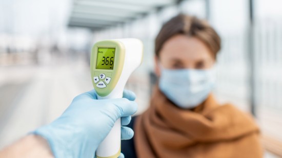 Hombre tomándole la temperatura a una mujer con mascarilla