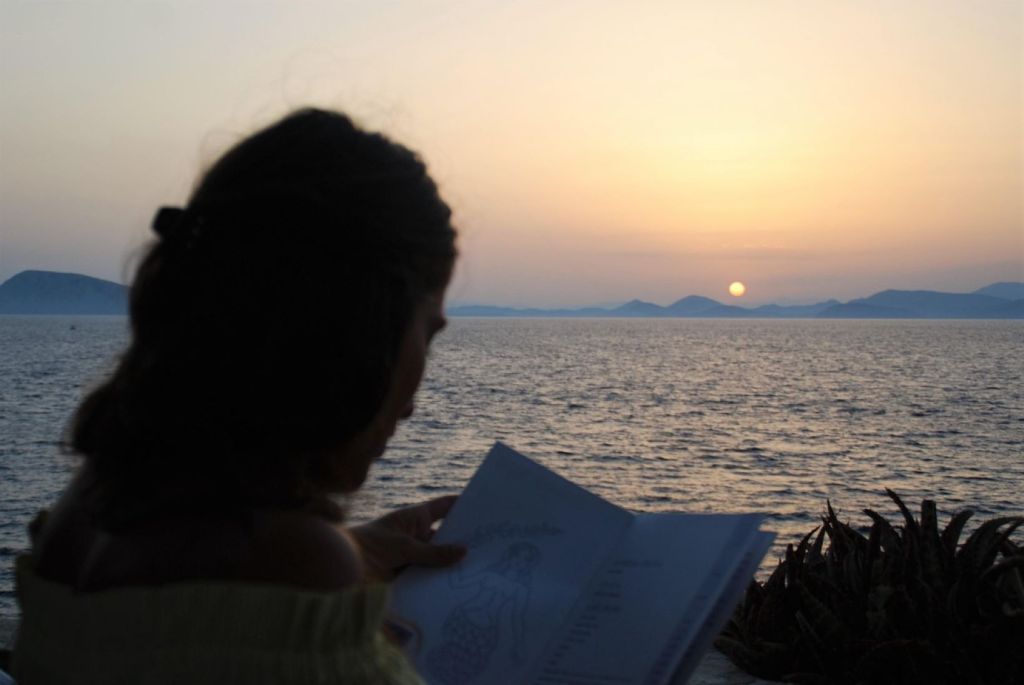 Uma mujer lee durante la puesta de sol en Grecia con el mar de fondo