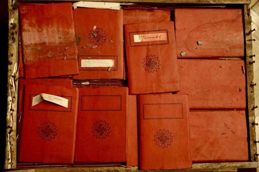Entre los documentos hallados en las cajas de madera se encontraban cuadernos de tapas rojas decoradas con esvásticas, cuidadosamente alineados como si aguardaran ser descubiertos